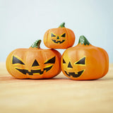 The Set of 3 Bumbu Toys Halloween Pumpkins placed on a wooden surface. The pumpkins all have black painted carving effect details.