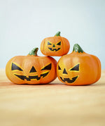The Set of 3 Bumbu Toys Halloween Pumpkins placed on a wooden surface. The pumpkins all have black painted carving effect details.