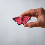 Bumbu Toys Wooden Butterfly in Pink, being held in an adult's hand.