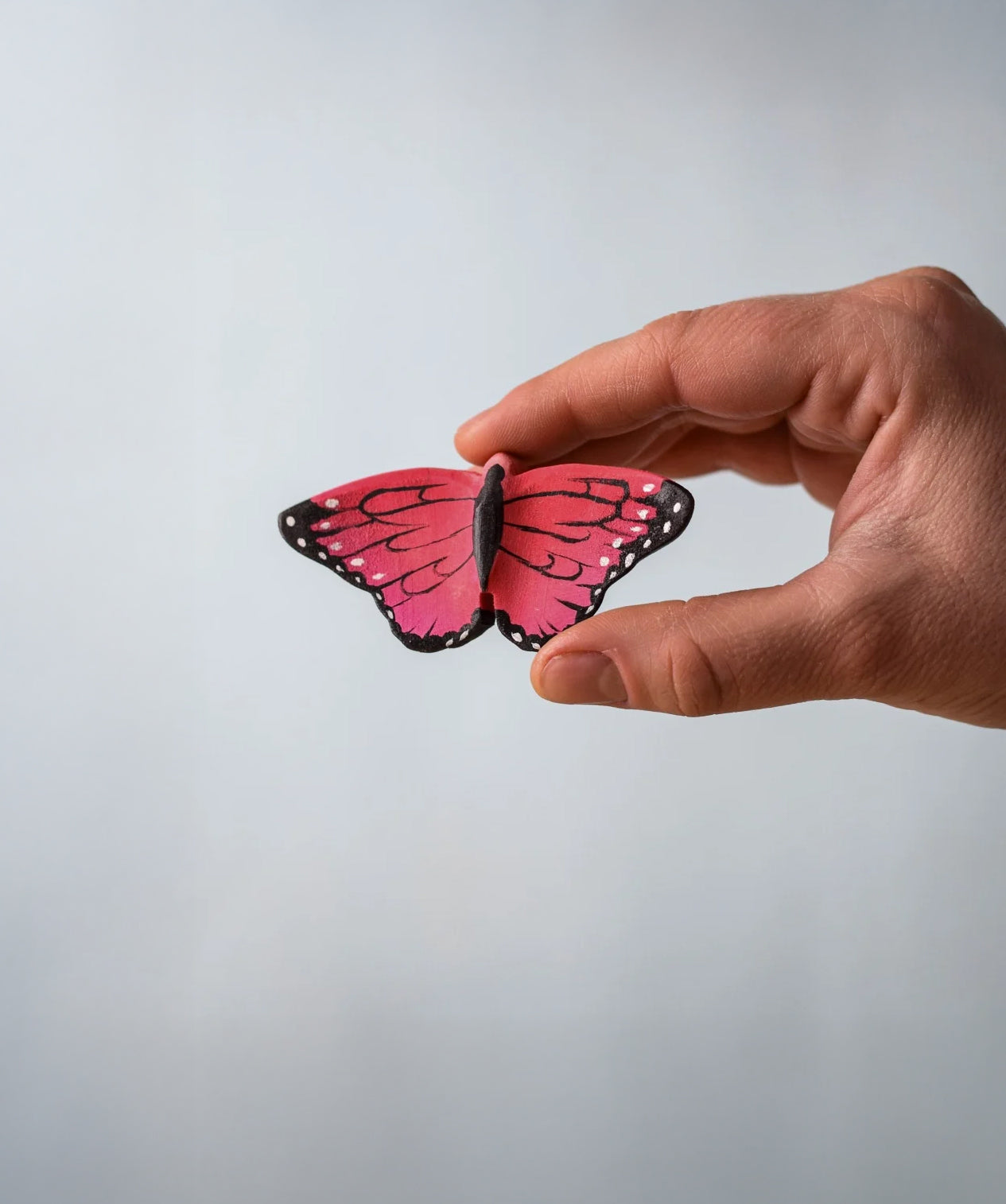 Bumbu Toys Wooden Butterfly in Pink, being held in an adult's hand.