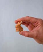 A hand holding The Bumbu Toys wooden baby rabbit figure, in a sitting position, for size reference