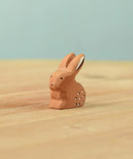 The Bumbu Toys wooden baby rabbit figure, in a sitting position