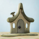 Bumbu Toys Witches house decorated with a Halloween theme. The house is grey in colour hand has cobwebs and a spider painted on. The House is placed on a wooden surface.