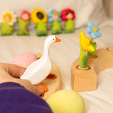 Adult hand holding a white Bumbu handcrafted goose decorative figure above a celebration ring 