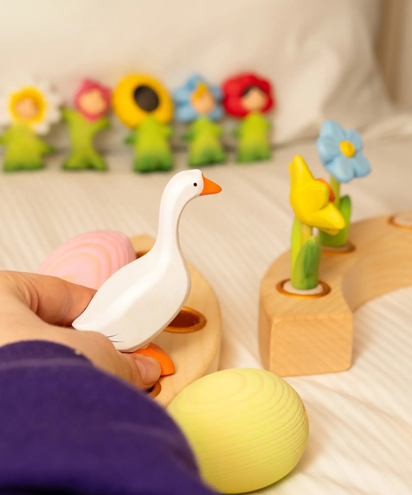 Adult hand holding a white Bumbu handcrafted goose decorative figure above a celebration ring 