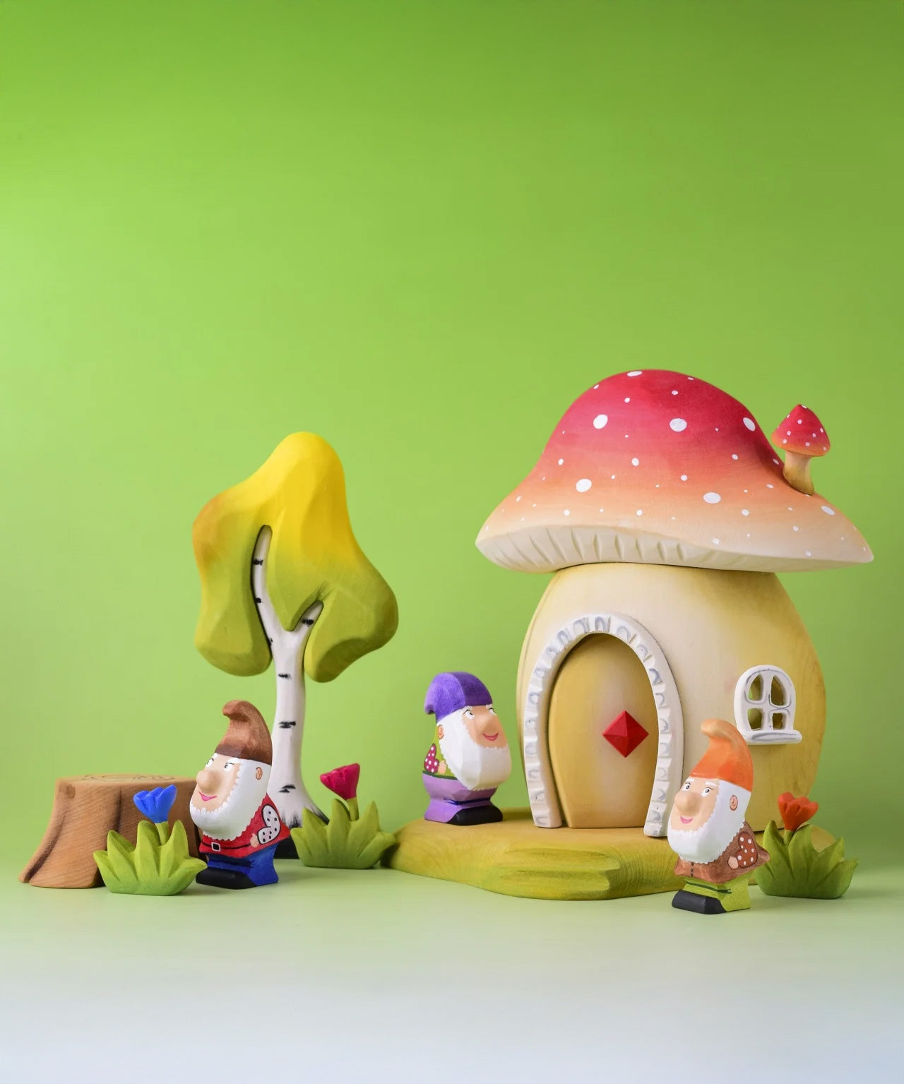 The Bumbu wooden toy dwarves shown in a small world play scene next to the Bumbu Toadstool house, flowers and birch tree. 
