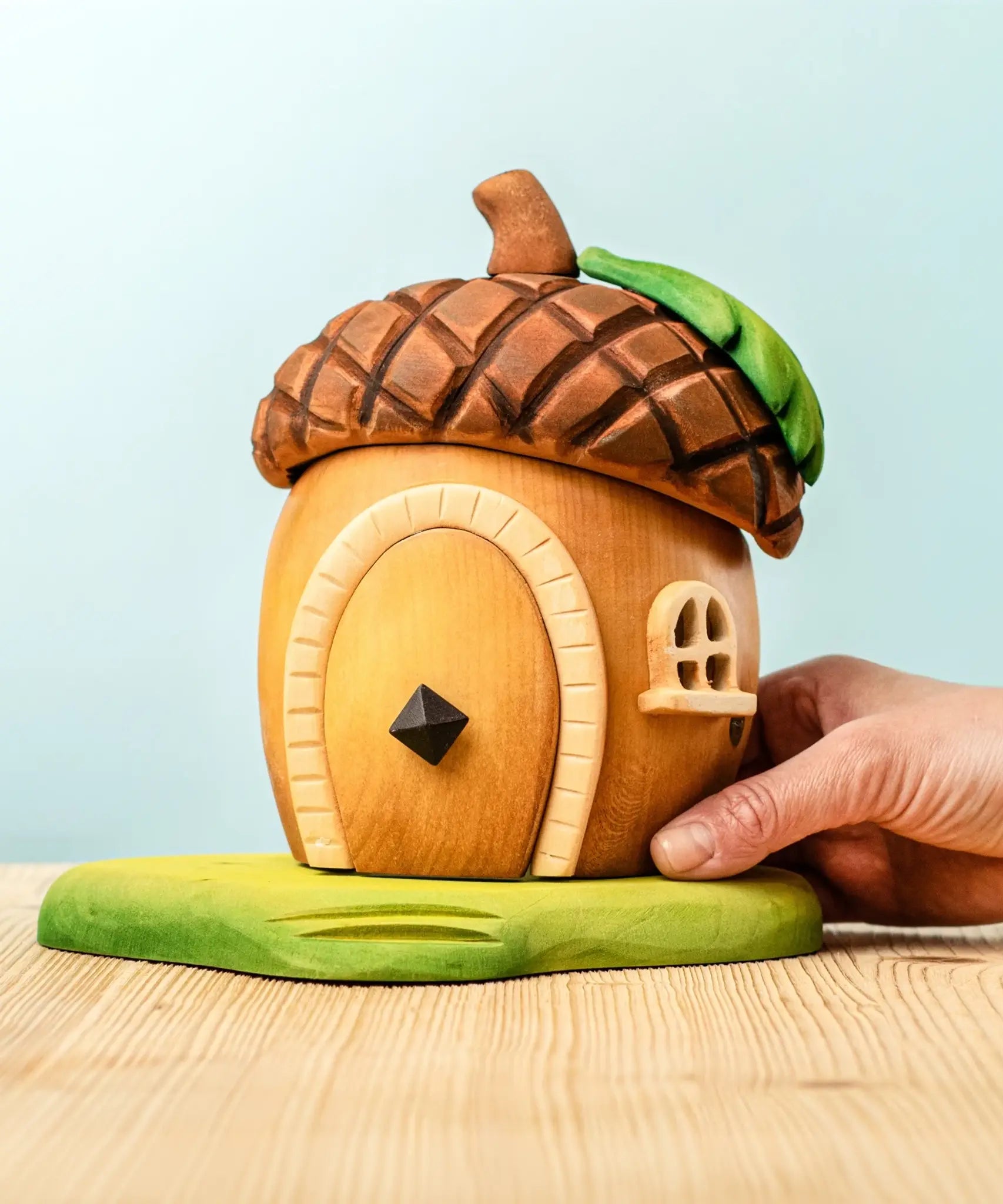 Adult hand holding the Bumbu toys handcrafted wooden acorn house showing scale