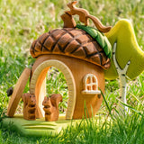 Bumbu toys handcrafted wooden acorn house with the removable door open, squirrel figures on the base and tree figure behind, standing in a grassy field