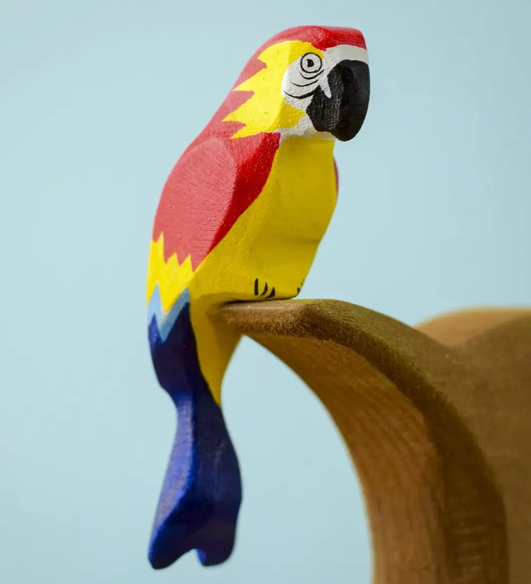 Bumbu toys handcrafted wooden Amazonian parrot figure with painted facial features perched on a branch