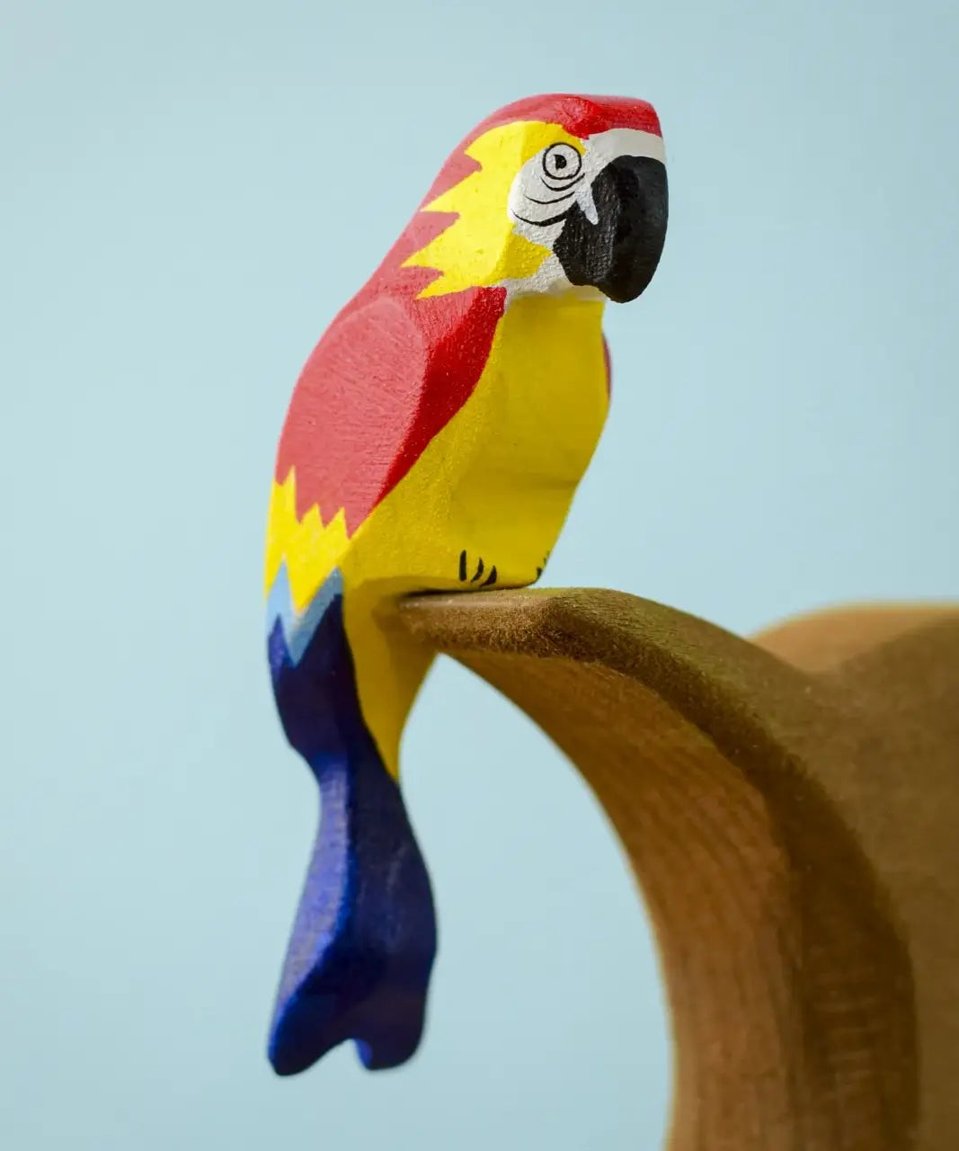 Bumbu toys handcrafted wooden Amazonian parrot figure with painted facial features perched on a branch
