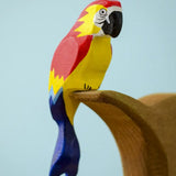 Bumbu toys handcrafted wooden Amazonian parrot figure with painted facial features perched on a branch