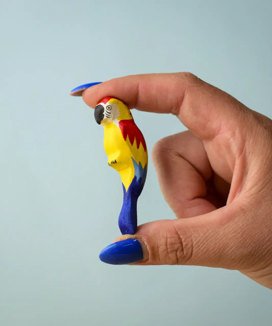 Adult hand holding a Bumbu toys handcrafted wooden blue macaw figure showing scale