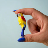 Adult hand holding a Bumbu toys handcrafted wooden blue macaw figure showing scale
