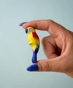 Adult hand holding a Bumbu toys handcrafted wooden blue macaw figure showing scale