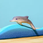 Bumbu Wooden Baby Dolphin. The toy is paired with a wave and sits on a wooden surface against a blue background.