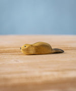 Bumbu wooden baby beaver figure resting on a wooden board.