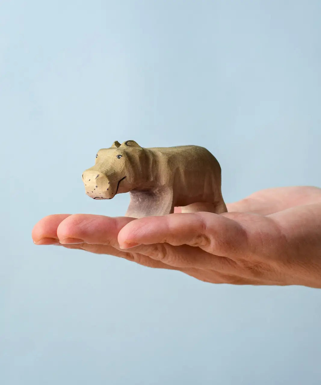 Bumbu toys handcrafted wooden grey standing baby hippo figure in a hand showing scale