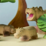Bumbu toys handcrafted wooden grey standing baby hippo figure in a playscene with trees in the background
