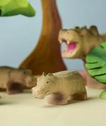Bumbu toys handcrafted wooden grey standing baby hippo figure in a playscene with trees in the background
