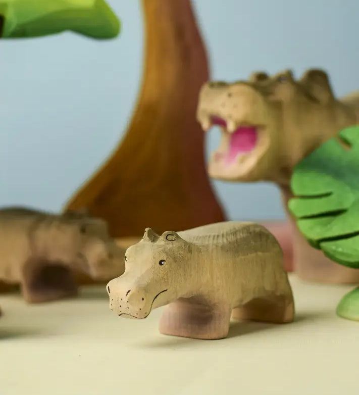 Bumbu toys handcrafted wooden grey standing baby hippo figure in a playscene with trees in the background