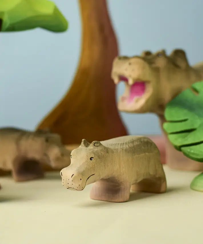 Bumbu toys handcrafted wooden grey standing baby hippo figure in a playscene with trees in the background