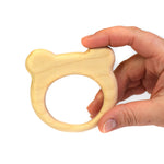 Close up of a hand holding the Bumbu plastic-free wooden bear baby teether on a white background