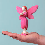 An adult balancing a Bumbu Wooden Blossom Fairy on their hand against a blue background.