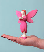 An adult balancing a Bumbu Wooden Blossom Fairy on their hand against a blue background.