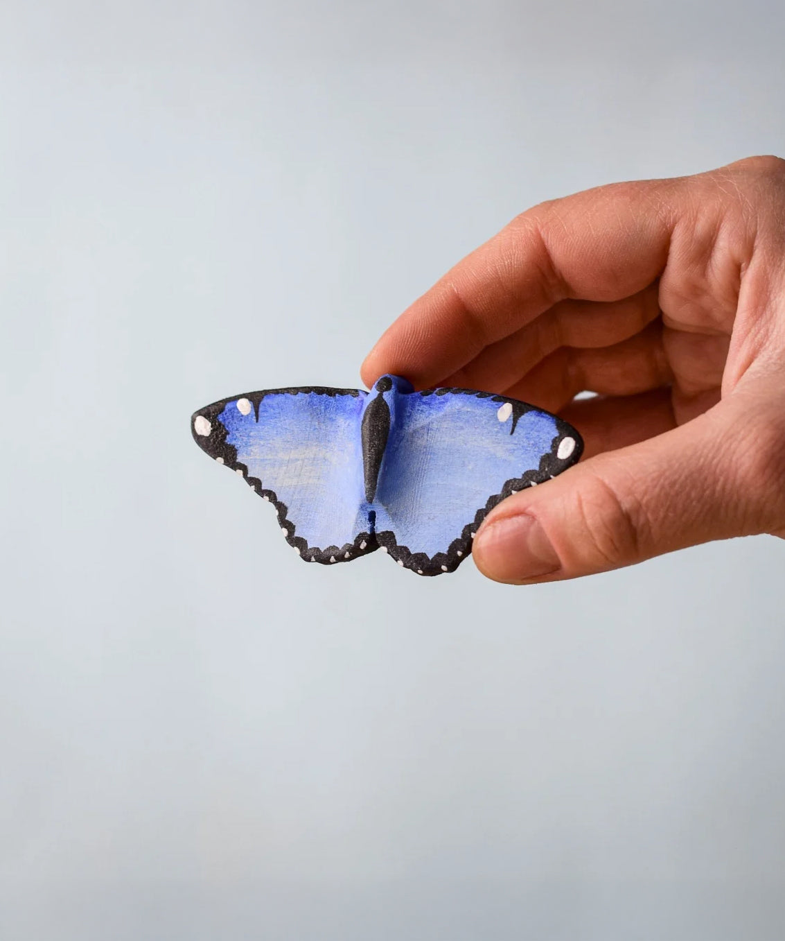 Bumbu Toys Wooden Butterfly in Blue, being held in an adult's hand.