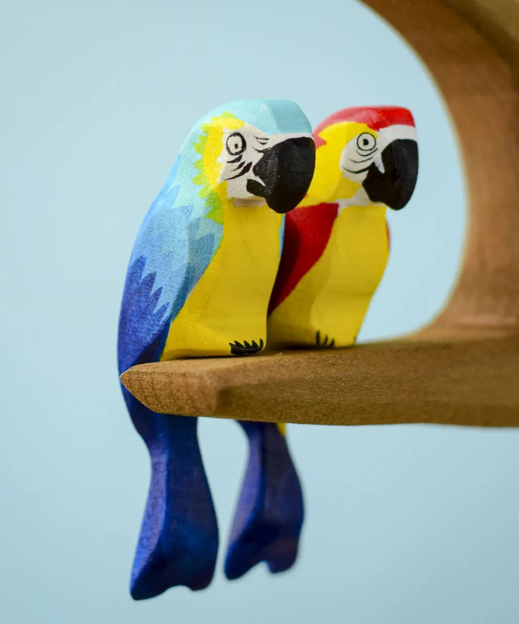 Bumbu toys handcrafted wooden blue macaw and a Amazonian parrot figure perched on a branch