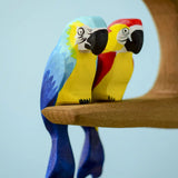 Bumbu toys handcrafted wooden blue macaw and a Amazonian parrot figure perched on a branch