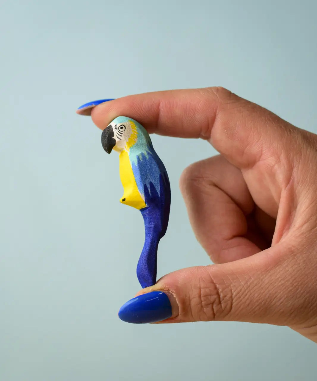 Adult hand holding a Bumbu toys handcrafted wooden blue macaw parrot figure showing scale