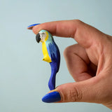 Adult hand holding a Bumbu toys handcrafted wooden blue macaw parrot figure showing scale