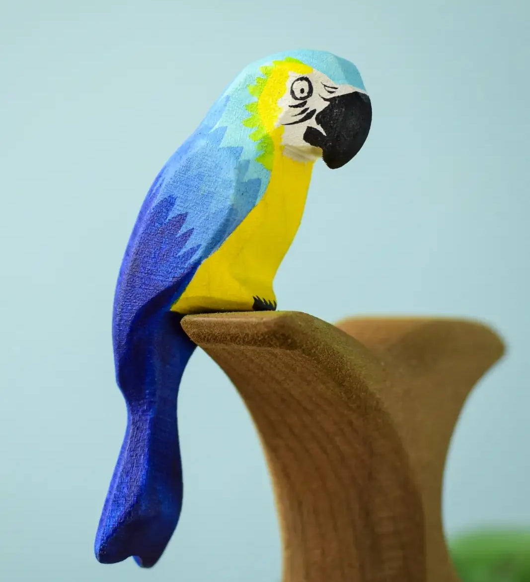 Bumbu toys handcrafted wooden blue macaw figure with painted facial features perched on a branch