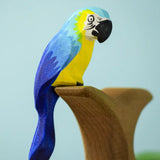 Bumbu toys handcrafted wooden blue macaw figure with painted facial features perched on a branch