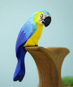 Bumbu toys handcrafted wooden blue macaw figure with painted facial features perched on a branch