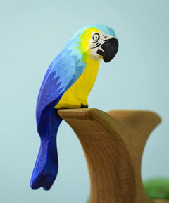 Bumbu toys handcrafted wooden blue macaw figure with painted facial features perched on a branch