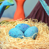 A set of Bumbu Wooden Brontosaurus Dinosaur Eggs in a nest. Dinosaurs and wooden trees can be seen in the background. 