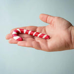 A hand holding the red and white wooden Bumbu candy cane