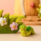 Bumbu handcrafted wooden green caterpillar figure standing next to a blossom bush figure