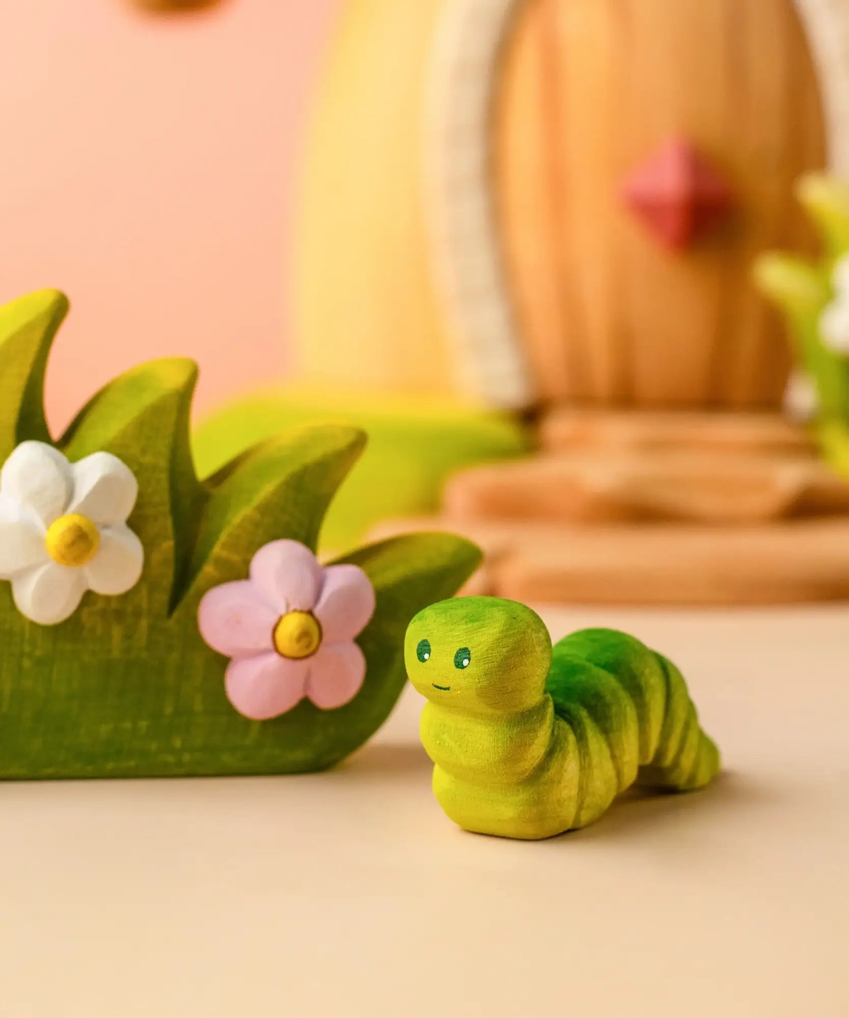 Bumbu handcrafted wooden green caterpillar figure standing next to a blossom bush figure