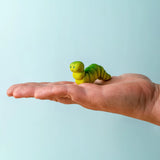 Adult hand holding a Bumbu handcrafted wooden green caterpillar figure showing scale