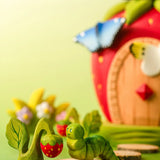 Bumbu handcrafted wooden green caterpillar figure next to a strawberry plant figure and a strawberry house in the backhground.