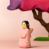 Bumbu handcrafted wooden cherry fairy figure in front of a pink blossom tree