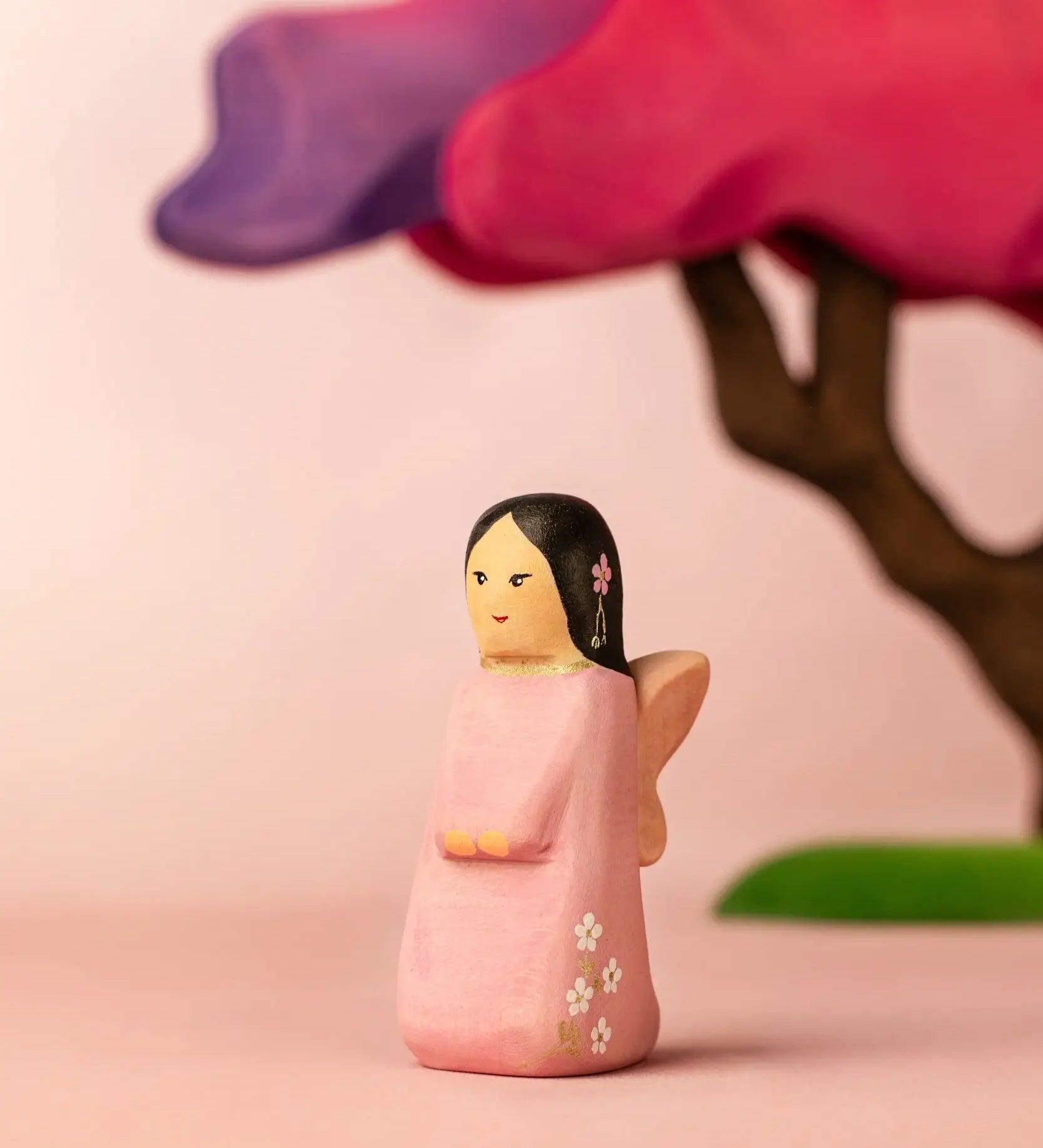 Bumbu handcrafted wooden cherry fairy figure in front of a pink blossom tree