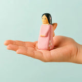Adult hand holding a Bumbu handcrafted wooden cherry fairy figure showing scale