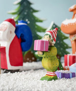 A Christmas scene including the Bumbu Santas elf holding a present, the Bumbu Santa and Christmas trees