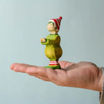 A hand holding the wooden Bumbu Santas elf wearing a red and white striped hat and a green outfit with its hands holding out to carry presents.