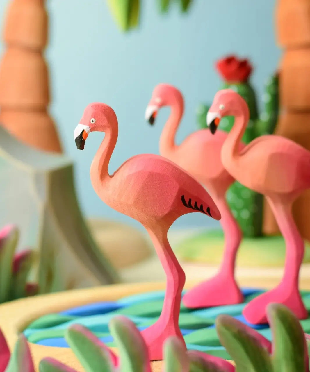 Play scene showing Bumbu handcrafted wooden pink flamingo figures, pond and tree sets in the backgroud.