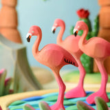 Play scene showing Bumbu handcrafted wooden pink flamingo figures, pond and tree sets in the backgroud.